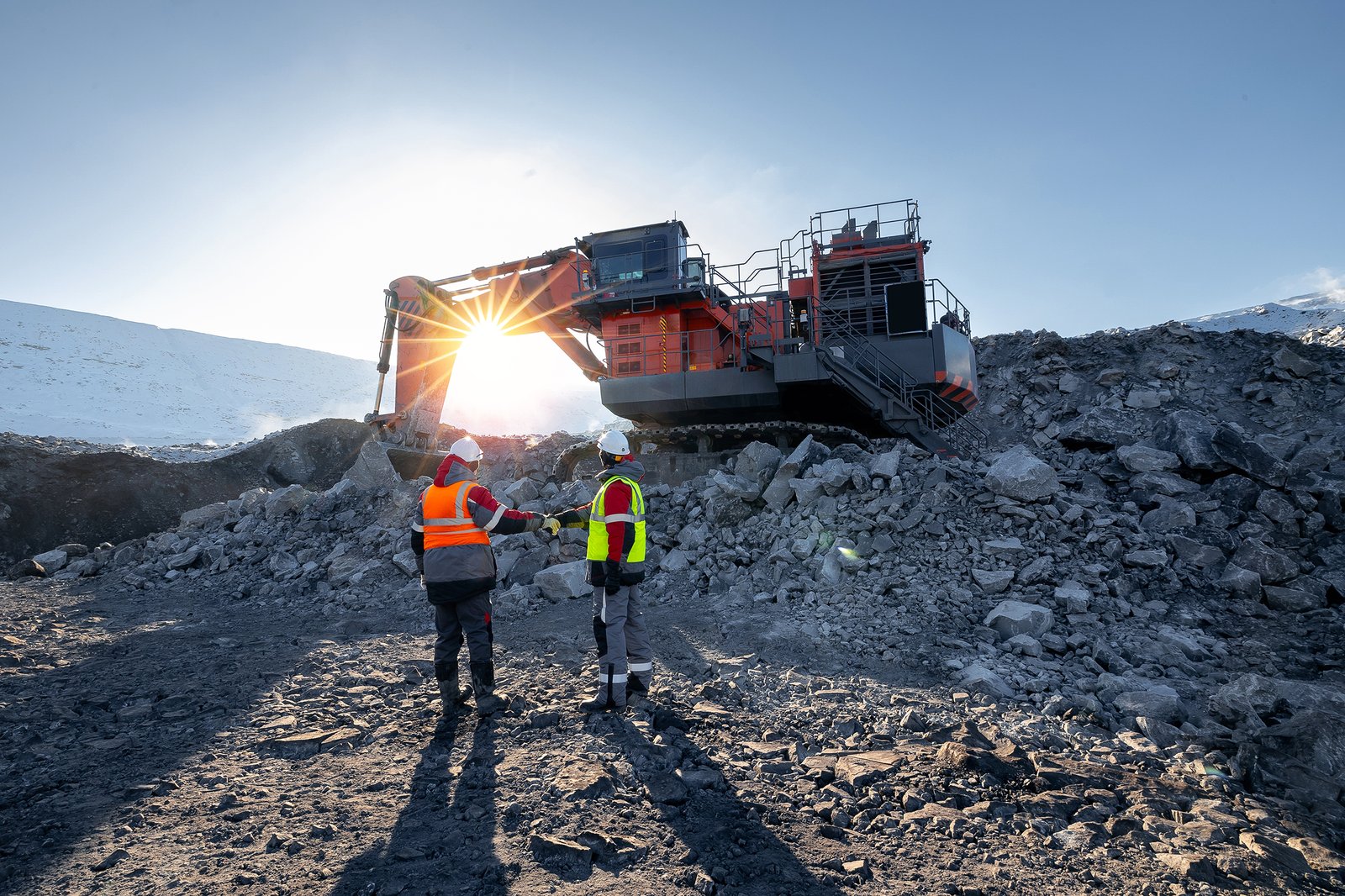 Two workers shaking hands at a mining site at sunrise